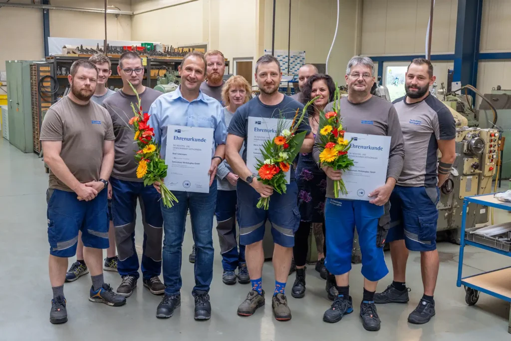 Gruppenfoto der Technotrans-Mitarbeiter, im Vordergrund René Liebermann, Mario Seifferth und Fredi Forkel jeweils mit Ehrenurkunde und einem Blumenstrauß zum Jubiläum